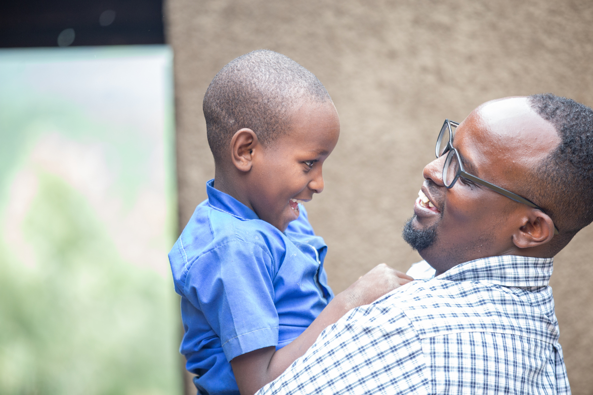 An East African man holds up a little boy smiling at each other